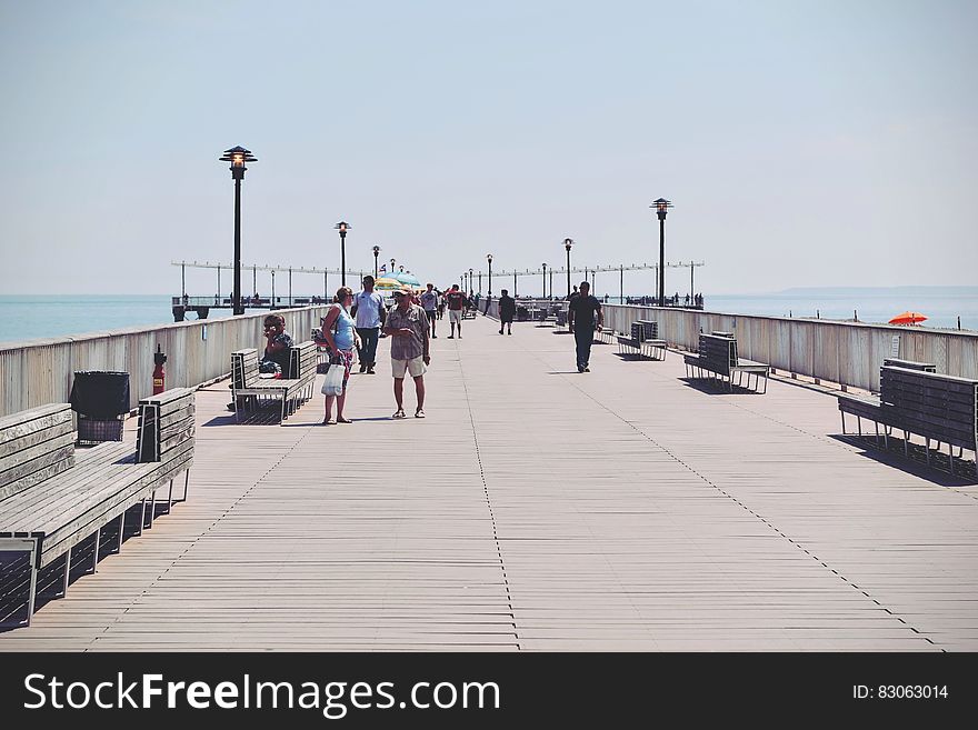 People Walking on a Beige Concrete Bridge Pathway Near Seashore during Daytime