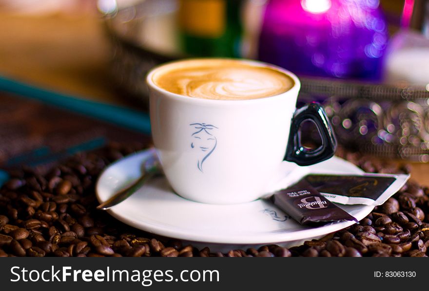 White china cup with coffee on saucer with roasted beans on wooden table. White china cup with coffee on saucer with roasted beans on wooden table.