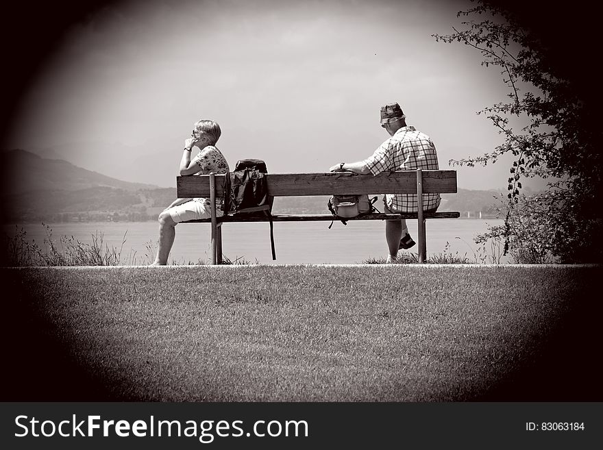 Man Sitting on Other Edge of Bench Parallel to Woman With Bags in Between Them