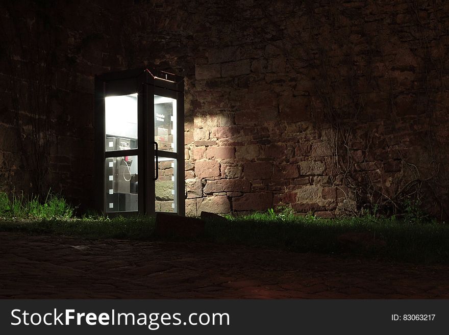 Telephone Booth Beside Brown Wall During Nighttime