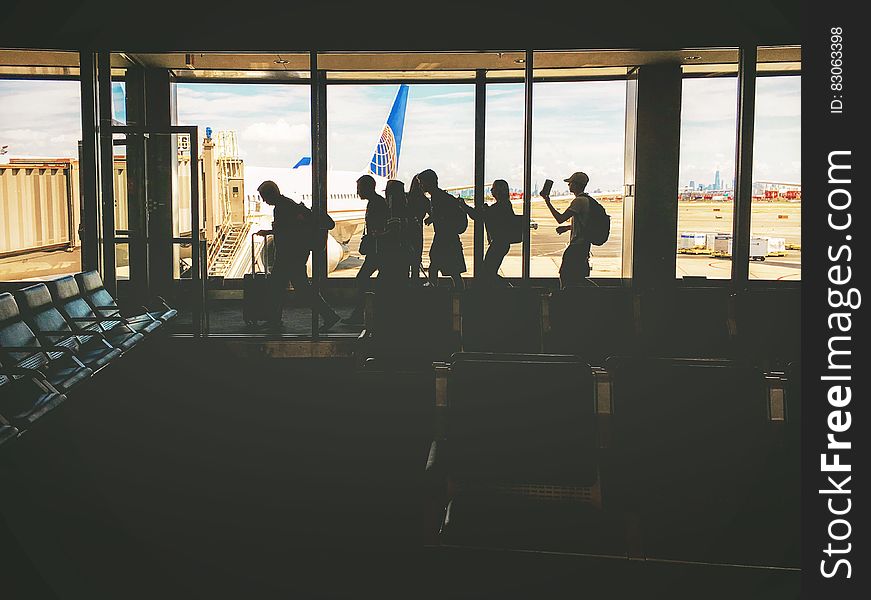 Group Of People Walking Near Clear Glass Window With A View Of White Airplane Parked During Daytime