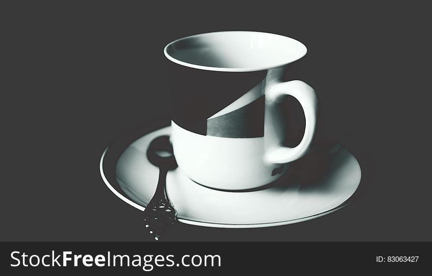 White and Black Ceramic Tea Mug on White Ceramic Round Plate and Stainless Steel Spoon on Top