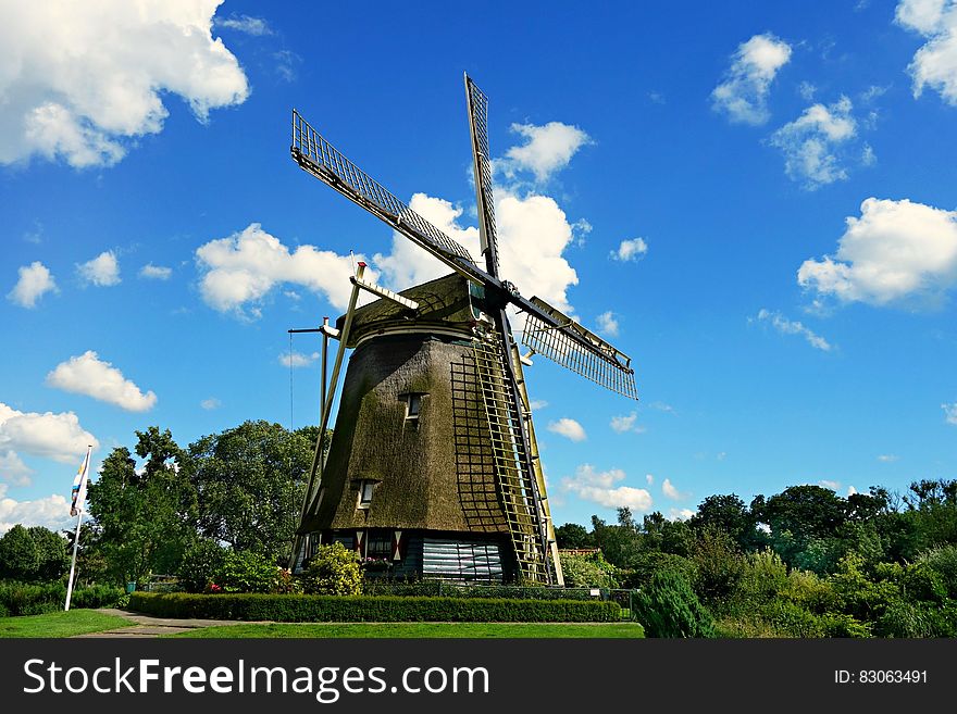 Brown and Black Windmill Under Cumulus Clouds Surrounded by Green Leaf Trees