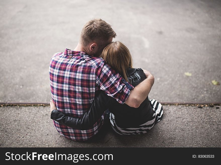 Man in Red White and Blue Check Long Sleeve Shirt Beside Woman in Black and White Stripes Shirt Hugging Each Other While Sitting o