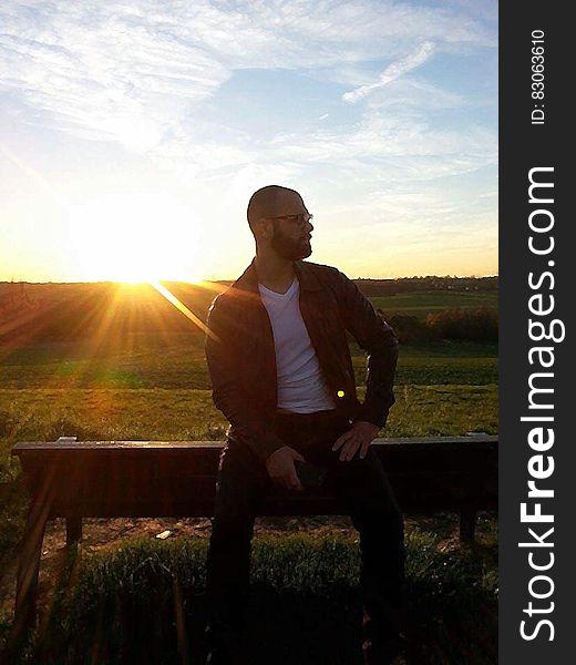 Portrait of man sitting on wooden fence in countryside at sunset. Portrait of man sitting on wooden fence in countryside at sunset.