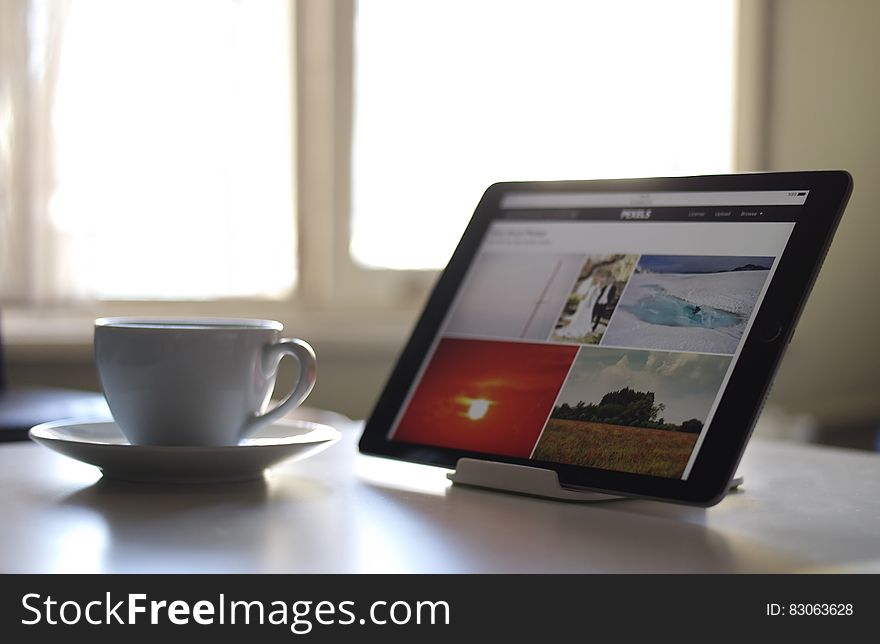 Black Tablet Computer Near a White Ceramic Teacup