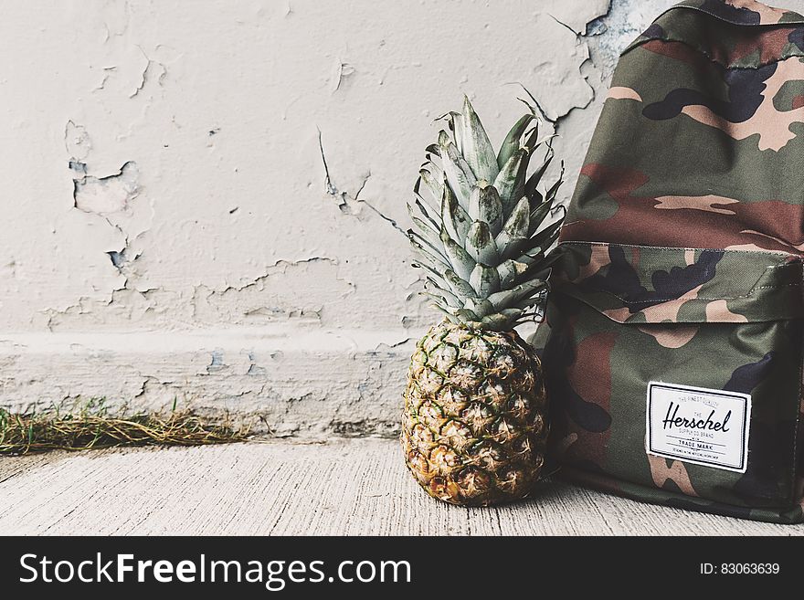 Camouflage backpack and fresh pineapple outdoors. Camouflage backpack and fresh pineapple outdoors.