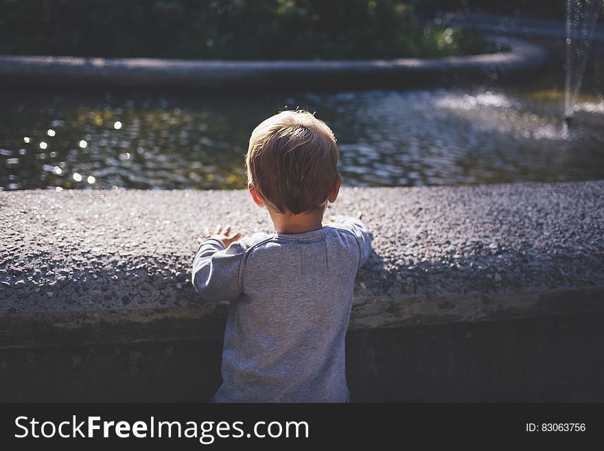 Boy in Gray Top Standing in Front of Water Fountain