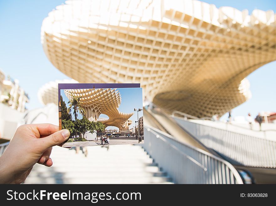 Person holding postcard in front of Metropol Parasol structure in Seville, Spain. Person holding postcard in front of Metropol Parasol structure in Seville, Spain