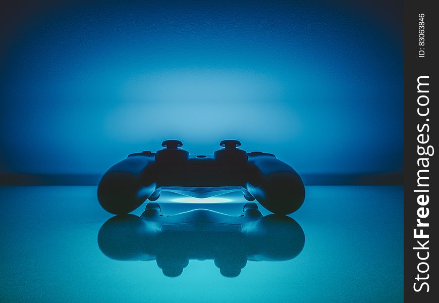 Dualshock gaming controller reflecting on blue background with copy space.