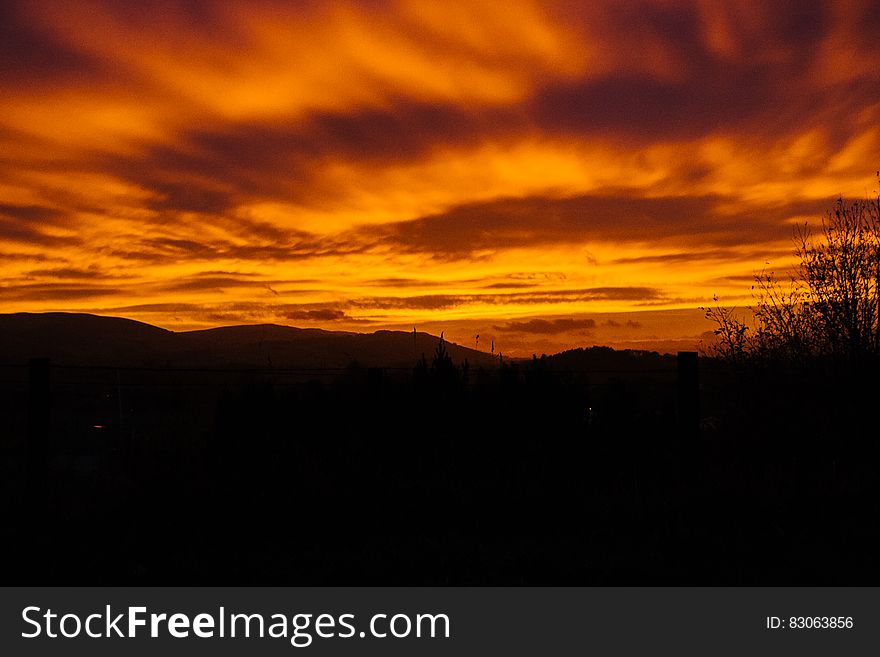 Scenic view of orange sunset and cloudscape over silhouetted countryside.
