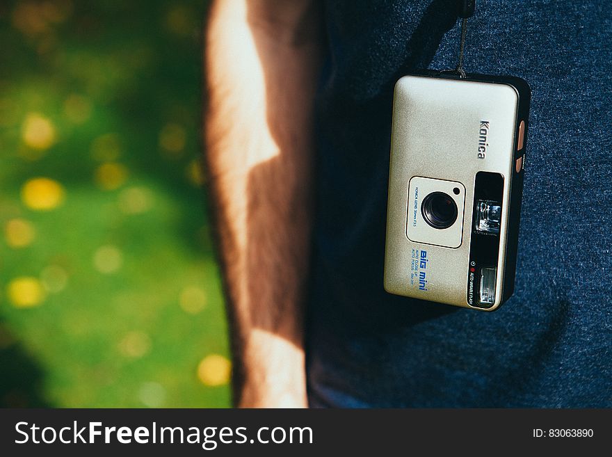 Konica camera hanging from strap from back on man outside.