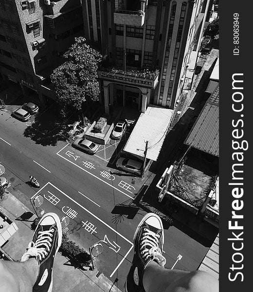 Grayscale Photography Man Wearing All Star Converse High Tops Below in Street and Building