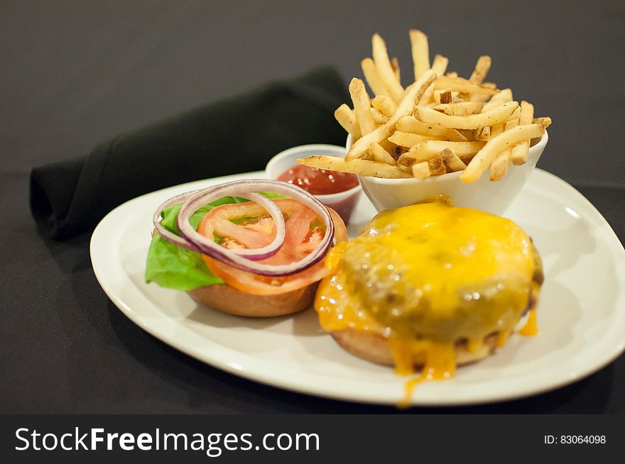 White plate with cheeseburger, hamburger, salad, chips and spicy sauce, black background. White plate with cheeseburger, hamburger, salad, chips and spicy sauce, black background.