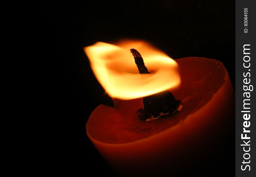 Closeup of candle burning bright in an orange saucer shaped candle holder, black background.