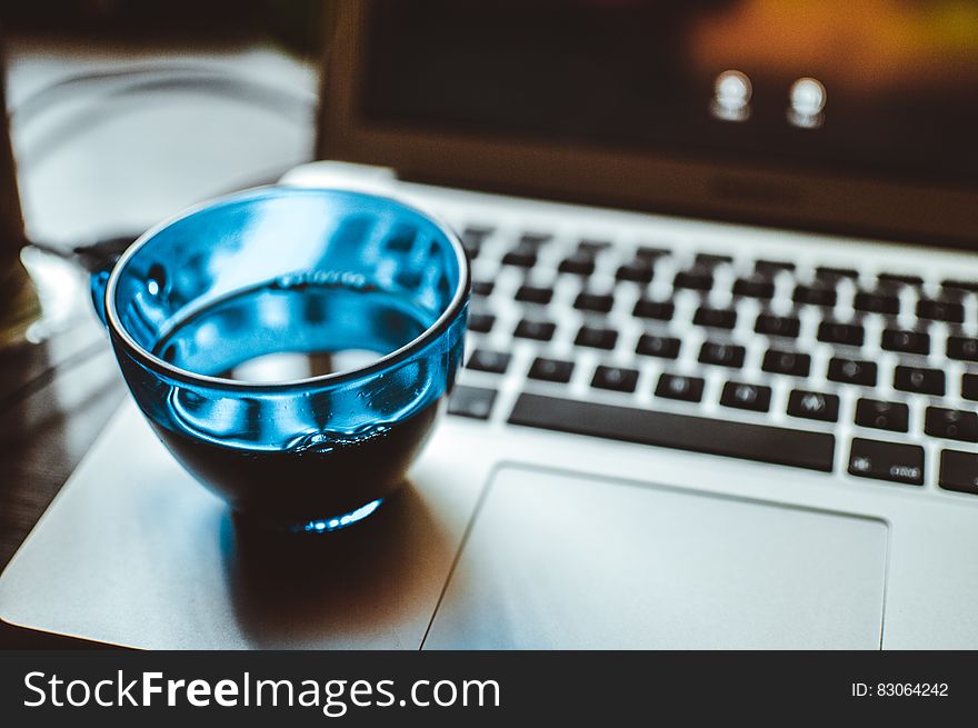 Shallow Focus Photography of Blue Glass Cup on Silver Laptop Computer