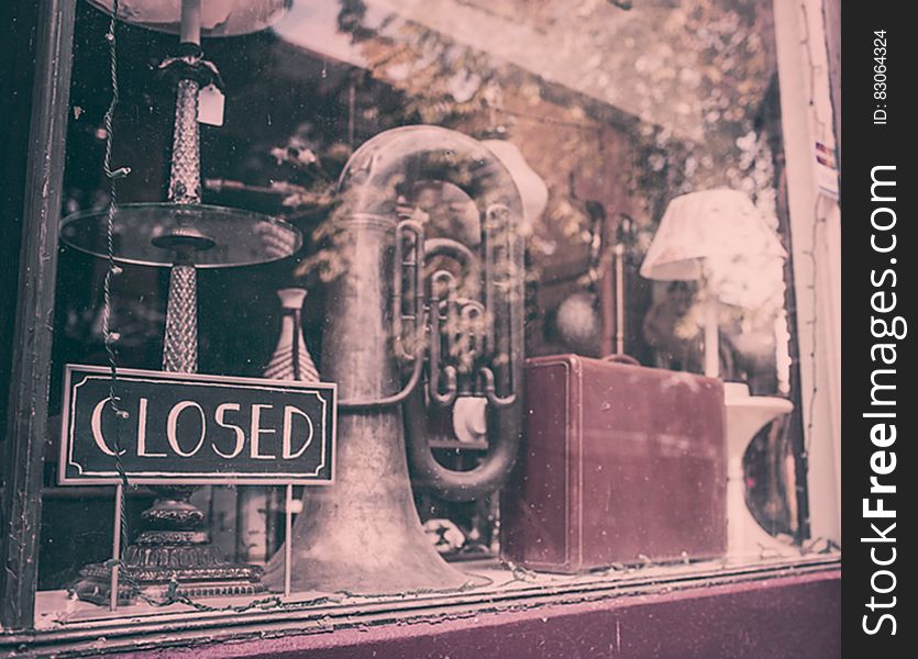 The window of an antique shop with tuba, suitcase and lamp.