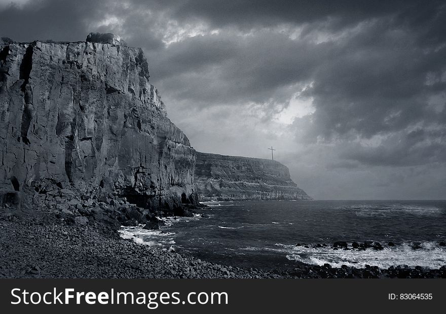 Cliff over rocky beach with waves in black and white.