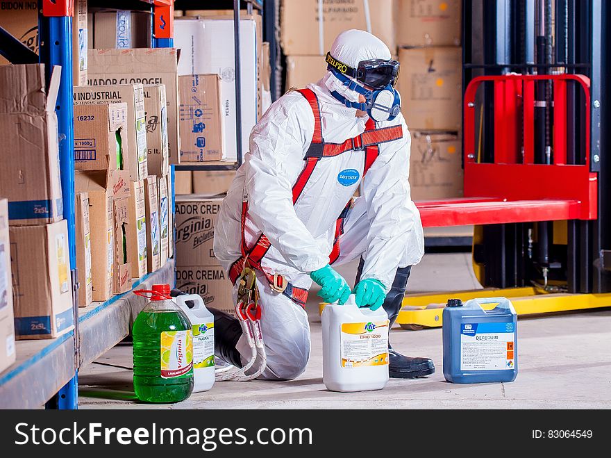 Worker in hazardous materials suit and ventilator handling industrial chemicals inside warehouse. Worker in hazardous materials suit and ventilator handling industrial chemicals inside warehouse.