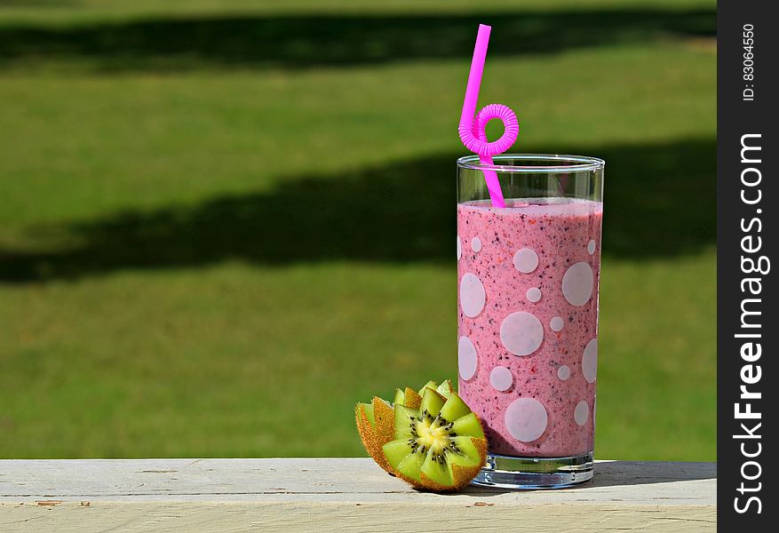 Close up of berry fruit drink in glass with straw and fresh kiwi on wooden railing outdoors on sunny day. Close up of berry fruit drink in glass with straw and fresh kiwi on wooden railing outdoors on sunny day.