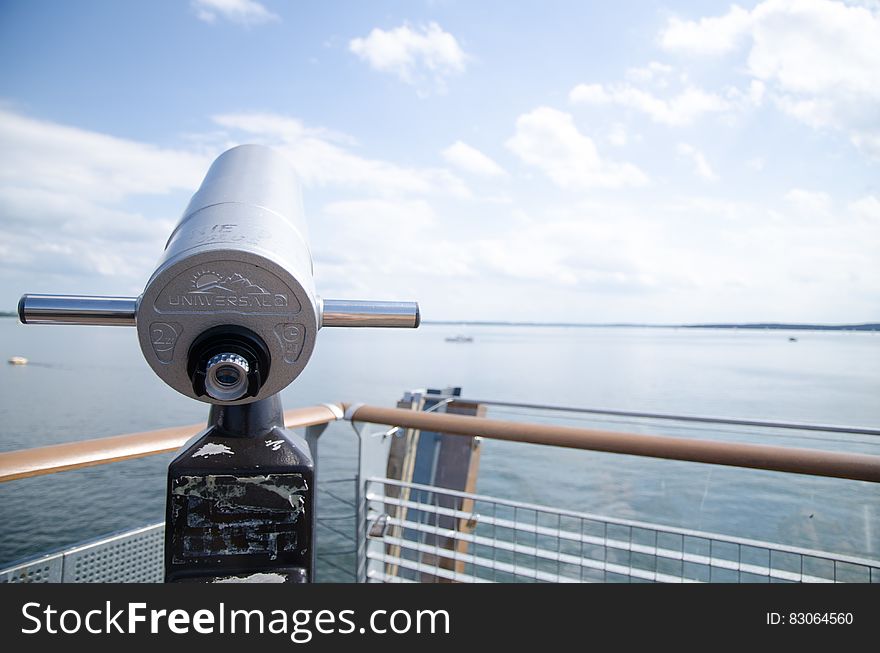 Tourist binoculars on pier along water with blue skies on sunny day in Poland. Tourist binoculars on pier along water with blue skies on sunny day in Poland.