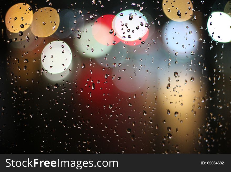 Colorful blur bokeh lights behind glass with raindrops at night. Colorful blur bokeh lights behind glass with raindrops at night.