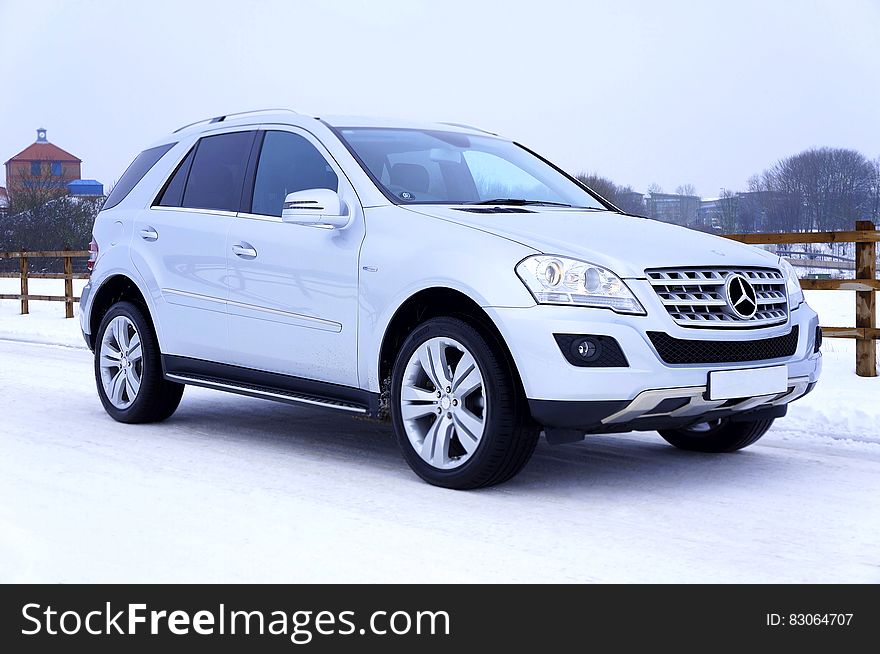 White Mercedes Benz SUV on snow covered roadway on sunny day.