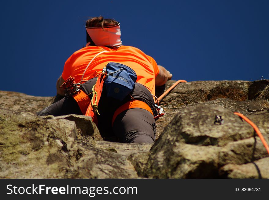 Person in Orange Shirt Climbing Rock during Daytime