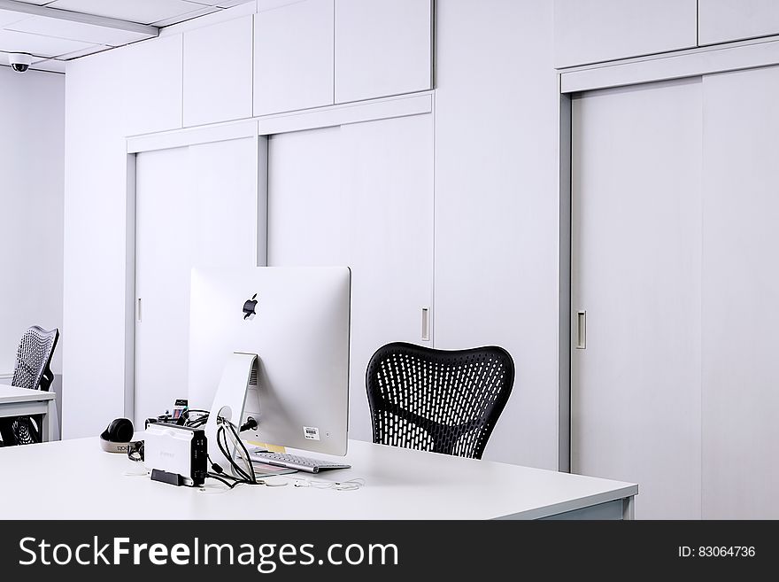 Black Mesh Office Rolling Chair Beside White Wooden Desk With White Imac