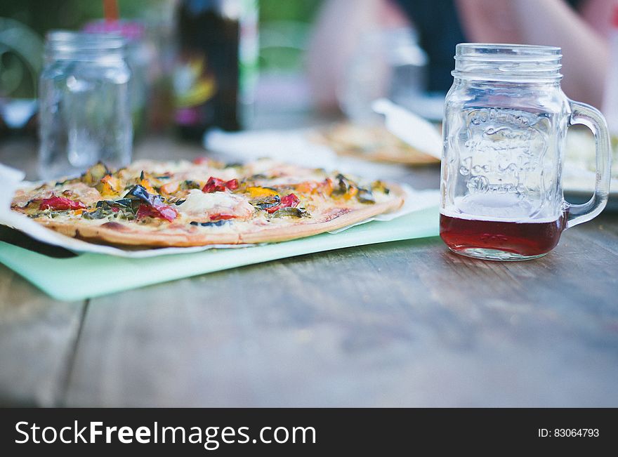 Whole pizza on cutting board with glass mason jars of tea on wooden table. Whole pizza on cutting board with glass mason jars of tea on wooden table.