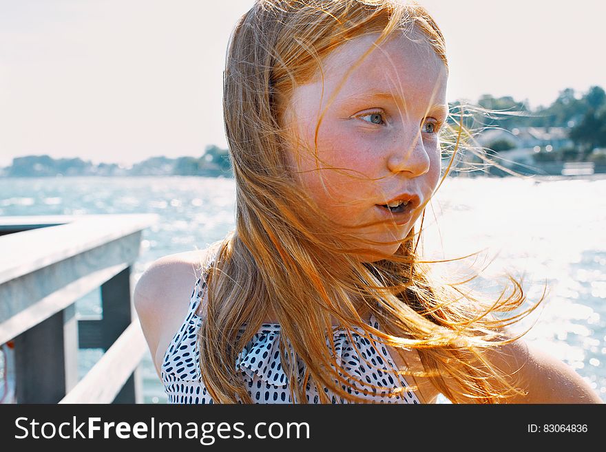 Portrait of blond girl on waterfront on sunny day.