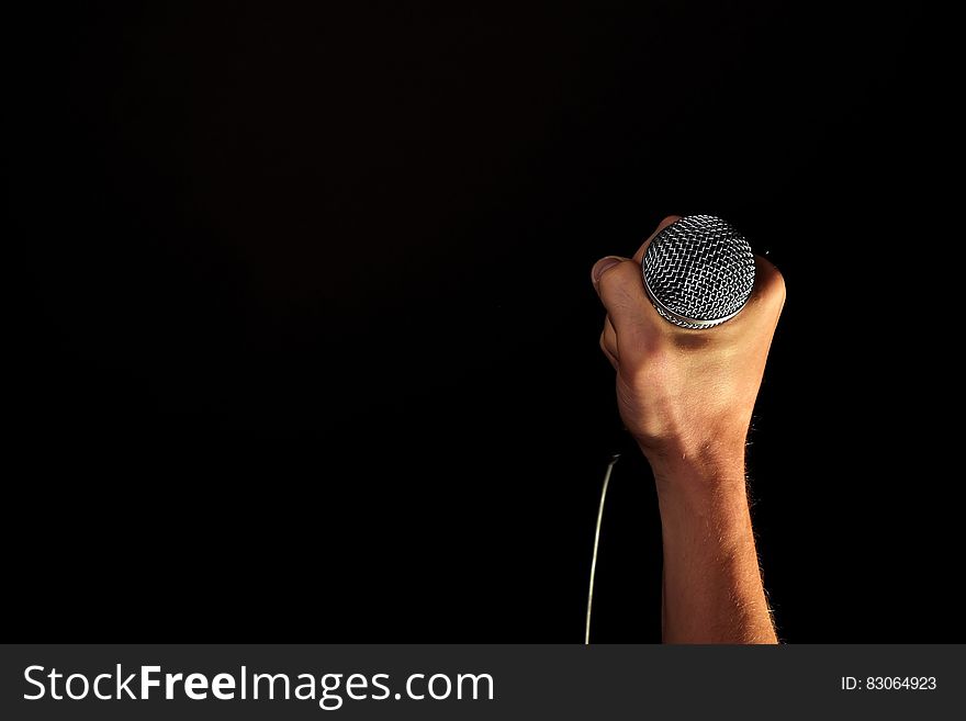 Close up of hand holding silver microphone on black with copy space. Close up of hand holding silver microphone on black with copy space.