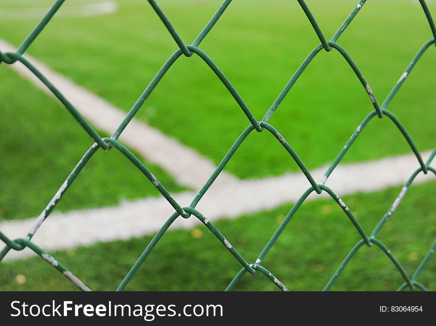 Close up of metal mesh fence around sports field on sunny day.