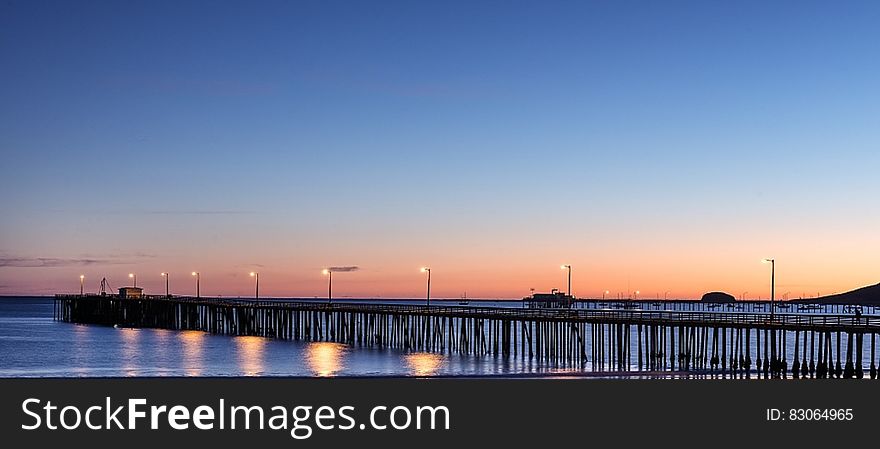 Sunset over ocean pier illuminated with streetlights.