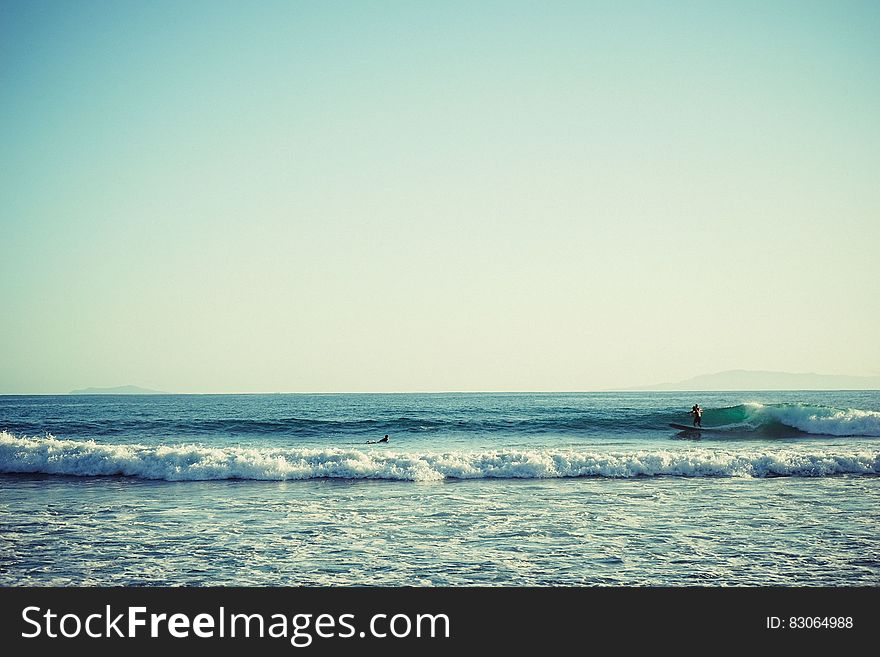 Surfer riding wave on ocean along seashore on sunny day. Surfer riding wave on ocean along seashore on sunny day.