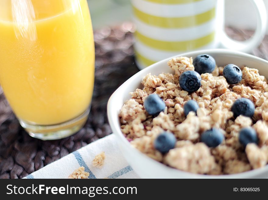 Bowl of granola cereal with blueberries, glass of orange juice and coffee cup.