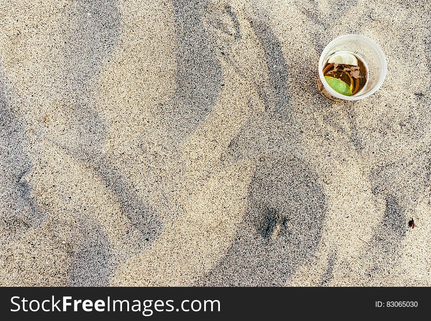 Overhead on plastic cup with drink on sandy beach on sunny day.