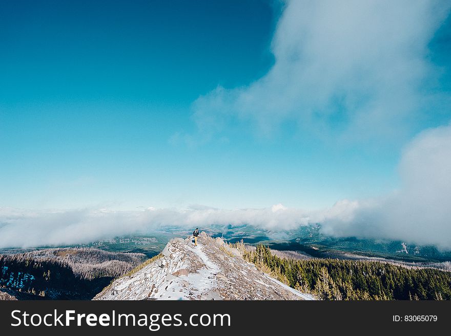 Hiker standing on snow capped mountain summit against blue skies on sunny day. Hiker standing on snow capped mountain summit against blue skies on sunny day.