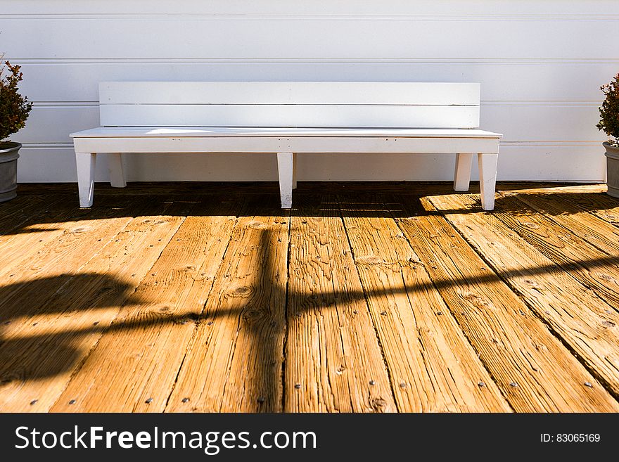 Empty white painted wooden bench on wooden plank deck on sunny day. Empty white painted wooden bench on wooden plank deck on sunny day.