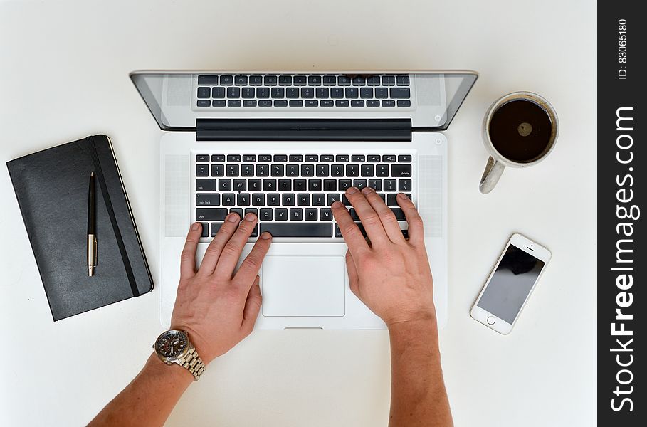 Overhead view of hands of worker typing on laptop with notebook, mobile and cup of coffee, white background. Overhead view of hands of worker typing on laptop with notebook, mobile and cup of coffee, white background.