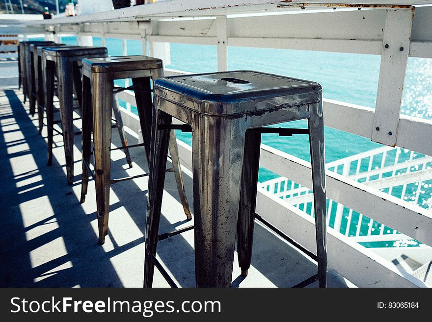 Row of wooden stools on outdoors balcony overlooking water. Row of wooden stools on outdoors balcony overlooking water.