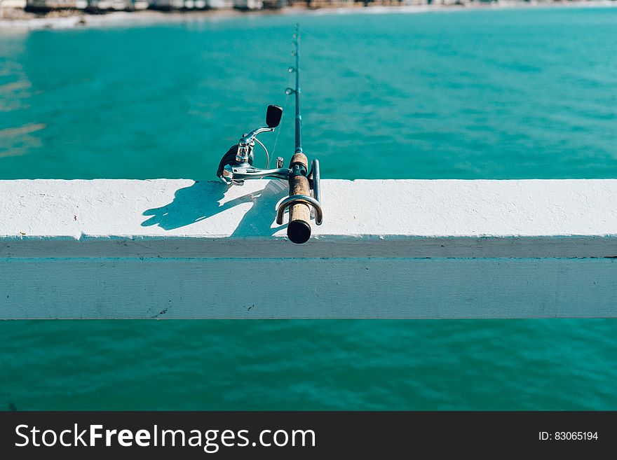 Fishing rod and reel on white fence overhanging sea. Fishing rod and reel on white fence overhanging sea.