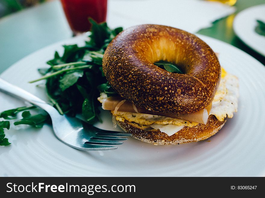 A bagel sandwich with fried egg and cheese and salad beside on a plate.