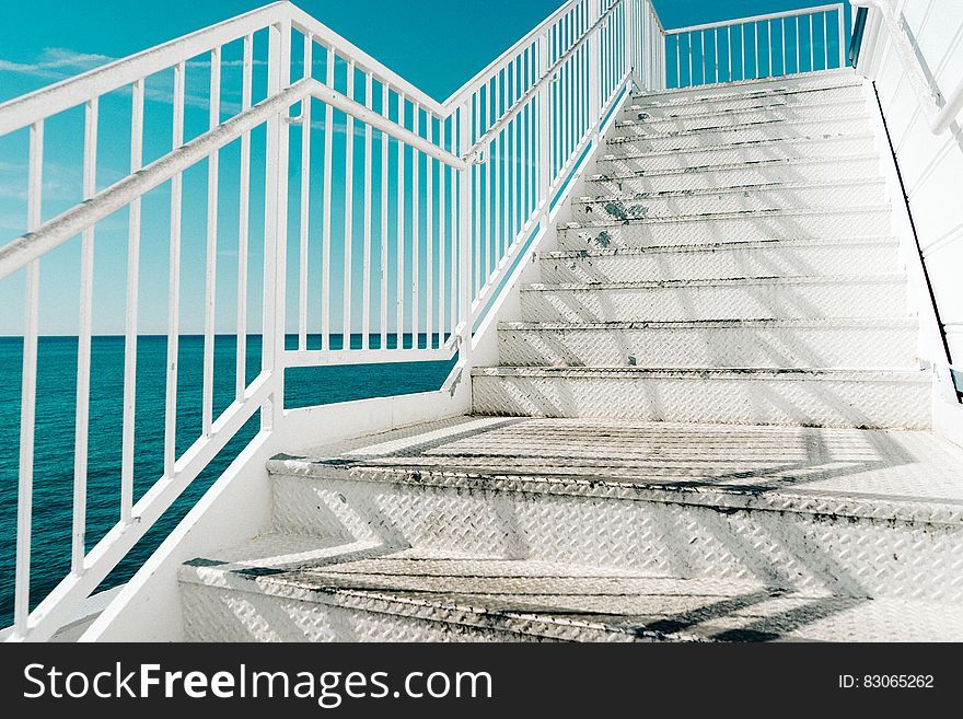 White outdoors staircase by the sea with blue sky background.