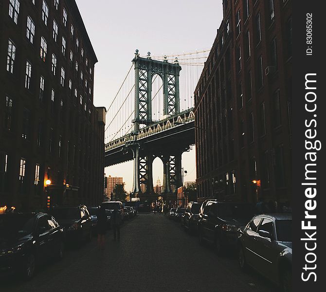 Brooklyn Bridge in New York city with cars parked on street in foreground, USA.