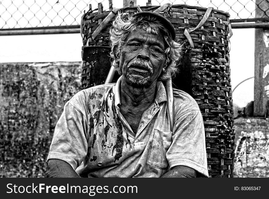 Man in Polo Shirt Sitting Near Brown Woven Basket Black and White Photography