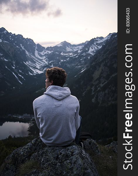 Man Wearing White Hoodie Sitting on a Rock With a View on Mountain