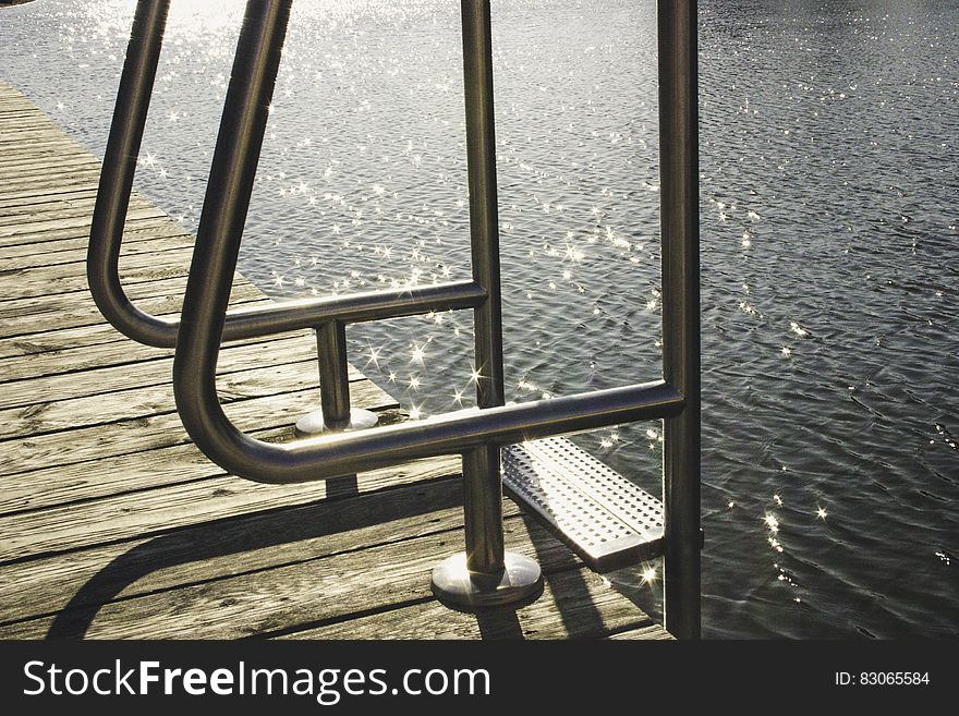 Metal ladder on wooden dock by glistening sea. Metal ladder on wooden dock by glistening sea.