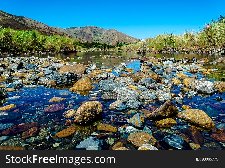 Stones at edge of picturesque lake with mountains and blue sky background.