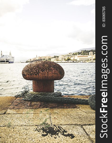 Old rope and mooring on dock with sea and large boat in background.